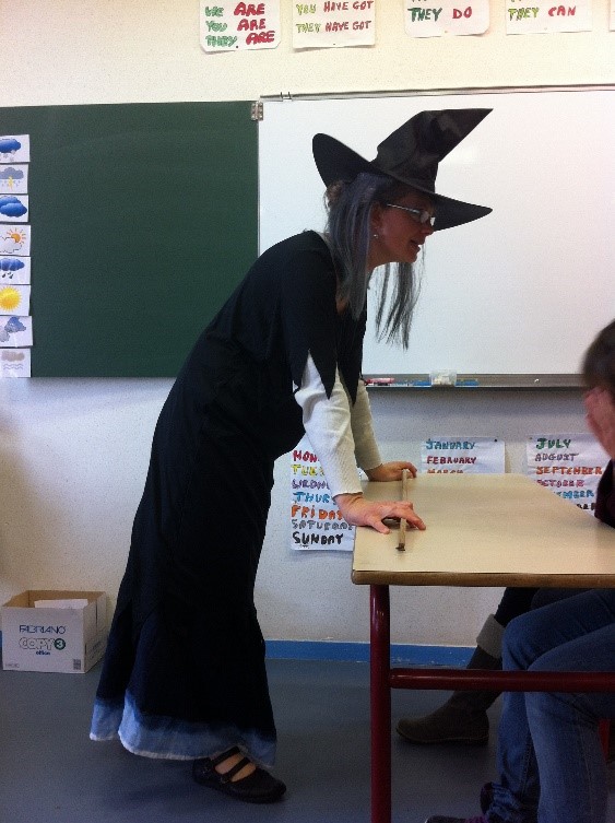 Photographie d’une personne déguisée en sorcière et parlant à une classe d’élèves.