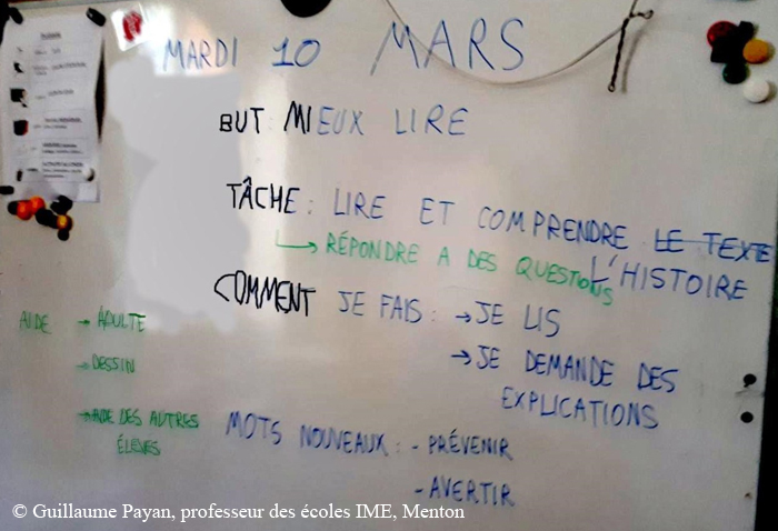 Sur un tableau sont écrits « But : mieux lire », « Tâche : lire et comprendre l’histoire / répondre à des questions », « Comment je fais : je lis / je demande des explications », « Mots nouveaux : prévenir, avertir », « Aide : adulte, dessin, aide des autres élèves ».