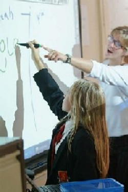 Une élève utilise le TBI à l'aide de son enseignante.